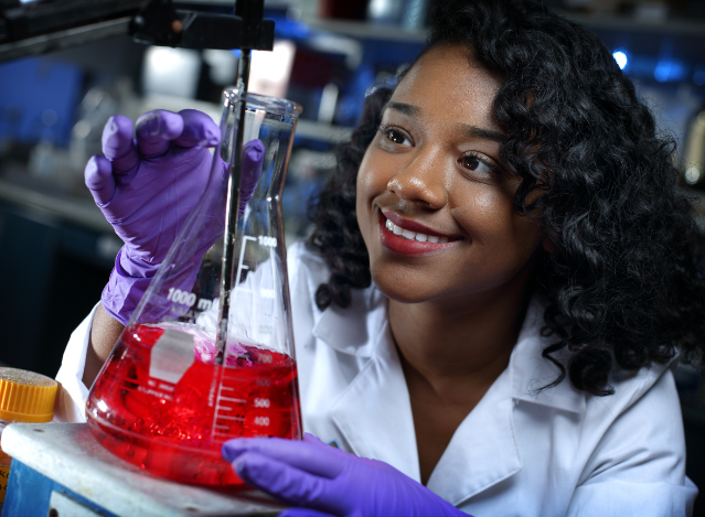 woman smiling while looking at a beaker full of red liquid